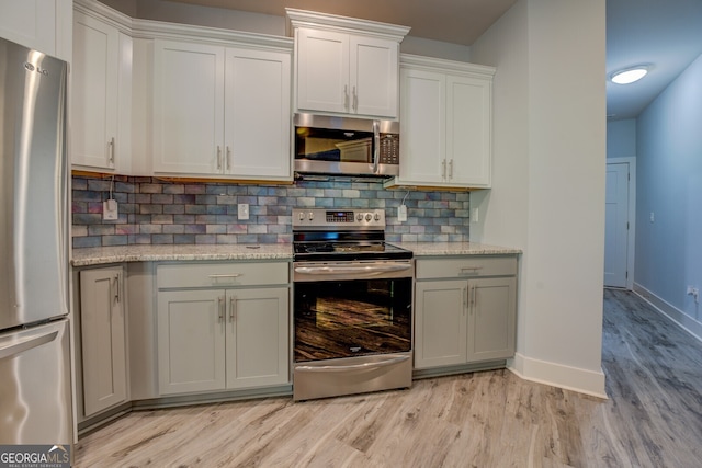 kitchen with backsplash, light stone counters, light wood-type flooring, and appliances with stainless steel finishes