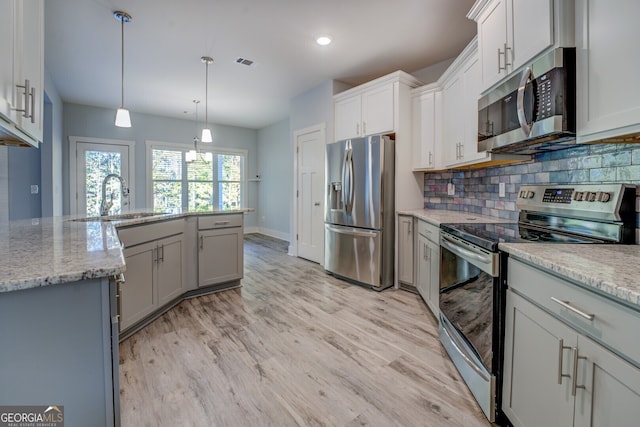 kitchen with light stone countertops, appliances with stainless steel finishes, sink, pendant lighting, and light hardwood / wood-style floors