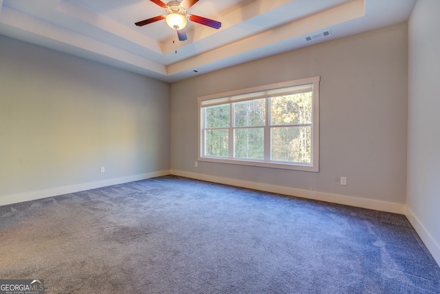 carpeted spare room featuring a tray ceiling and ceiling fan