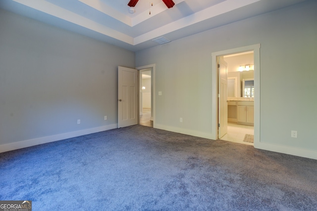 unfurnished bedroom with a raised ceiling, ensuite bath, ceiling fan, and carpet floors