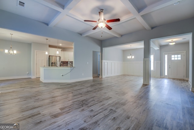 unfurnished living room with ceiling fan with notable chandelier, beam ceiling, and light hardwood / wood-style flooring