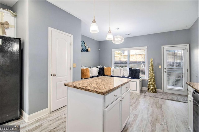 kitchen with white cabinetry, light hardwood / wood-style flooring, pendant lighting, black refrigerator, and a kitchen island