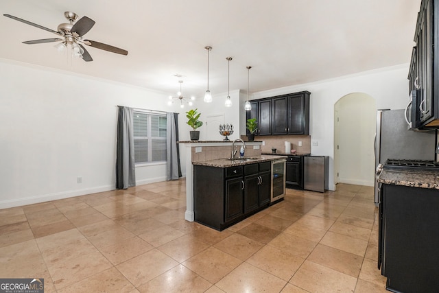 kitchen with pendant lighting, a kitchen island with sink, crown molding, wine cooler, and light stone counters