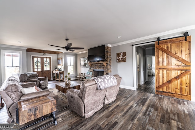 living room featuring ceiling fan, a barn door, a stone fireplace, dark hardwood / wood-style floors, and crown molding