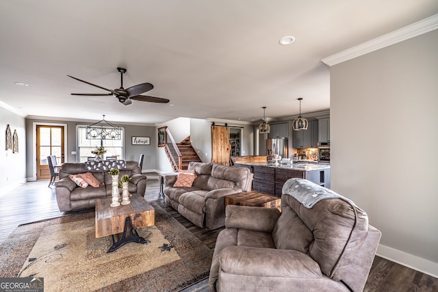 living room with ornamental molding, a barn door, ceiling fan, and dark wood-type flooring