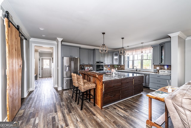 kitchen with appliances with stainless steel finishes, tasteful backsplash, light stone counters, a barn door, and a center island