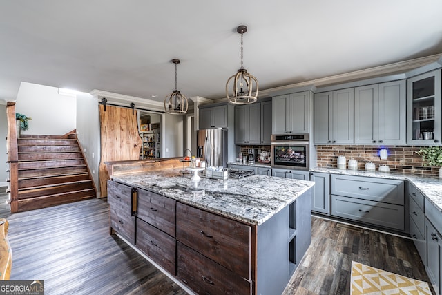 kitchen featuring a barn door, light stone counters, appliances with stainless steel finishes, decorative light fixtures, and dark hardwood / wood-style flooring