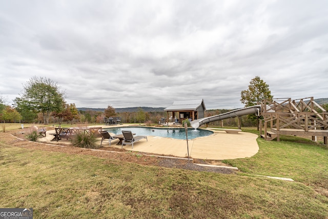 view of swimming pool featuring a lawn, a water slide, and a patio