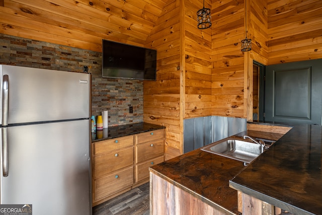 kitchen with pendant lighting, dark wood-type flooring, sink, wooden walls, and stainless steel refrigerator