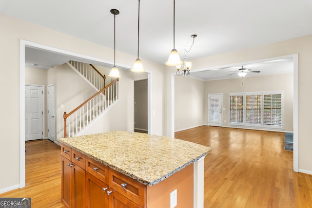 kitchen with light stone countertops, decorative light fixtures, a kitchen island, and light hardwood / wood-style floors