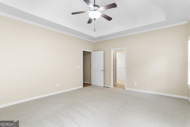 empty room with a raised ceiling, light carpet, ceiling fan, and ornamental molding