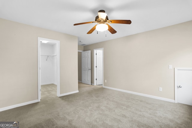 unfurnished bedroom featuring a spacious closet, a closet, ceiling fan, and light carpet