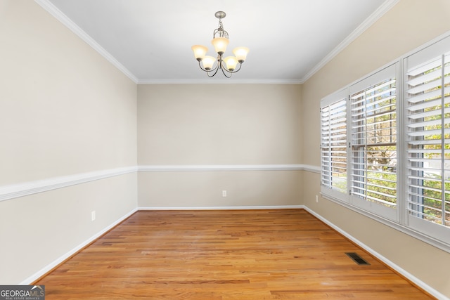 empty room with a notable chandelier, a healthy amount of sunlight, light hardwood / wood-style floors, and ornamental molding