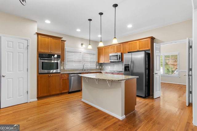 kitchen featuring light stone countertops, stainless steel appliances, sink, light hardwood / wood-style flooring, and a center island