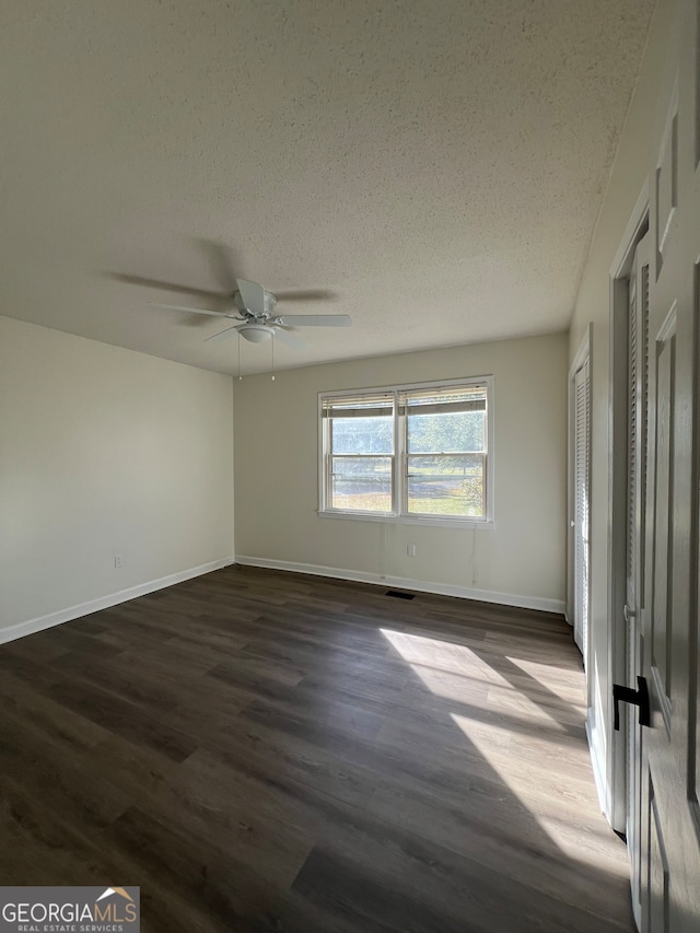 unfurnished room with ceiling fan, dark wood-type flooring, and a textured ceiling