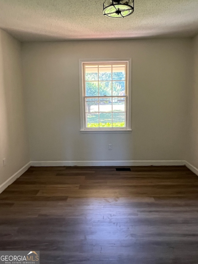 spare room featuring dark hardwood / wood-style flooring and a textured ceiling