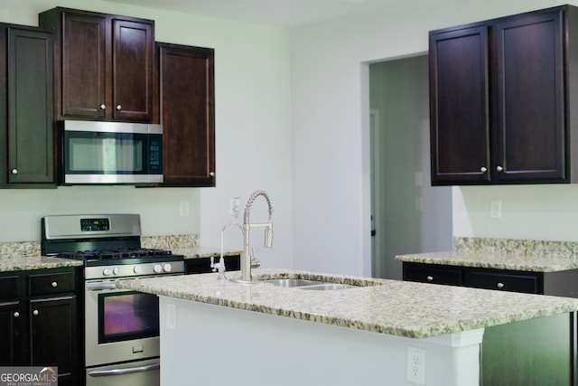 kitchen featuring light stone counters, dark brown cabinetry, stainless steel appliances, sink, and an island with sink