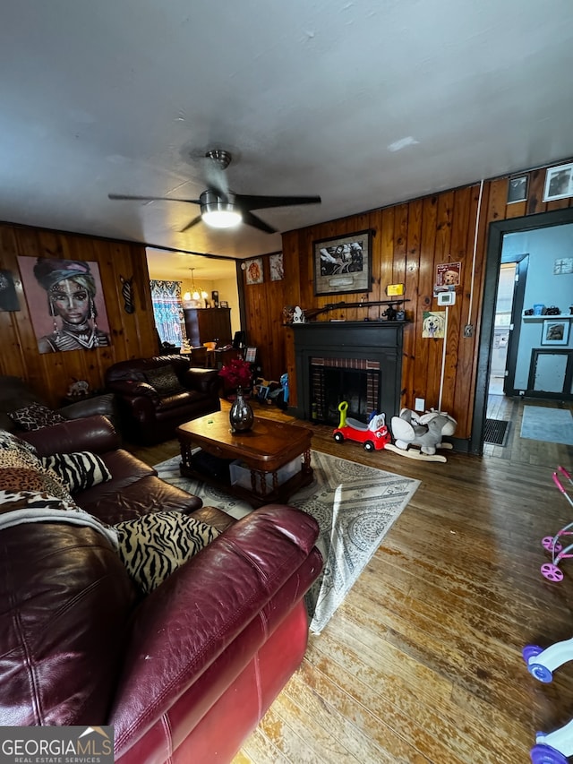 living room with hardwood / wood-style floors, ceiling fan, wood walls, and a fireplace