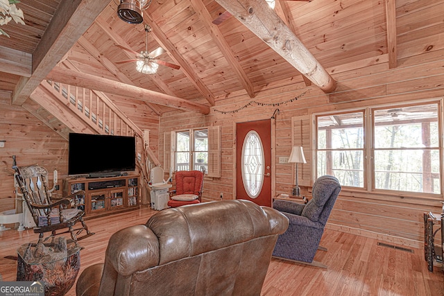 living room with vaulted ceiling with beams, wood walls, plenty of natural light, and light wood-type flooring