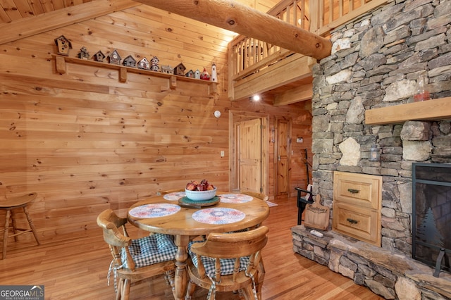 dining area with beamed ceiling, light wood-type flooring, a fireplace, and wood walls