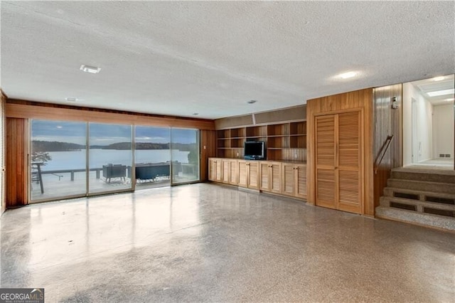 unfurnished living room featuring wood walls, a textured ceiling, and a water view