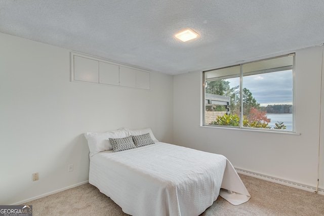 carpeted bedroom with a water view, a baseboard radiator, and a textured ceiling