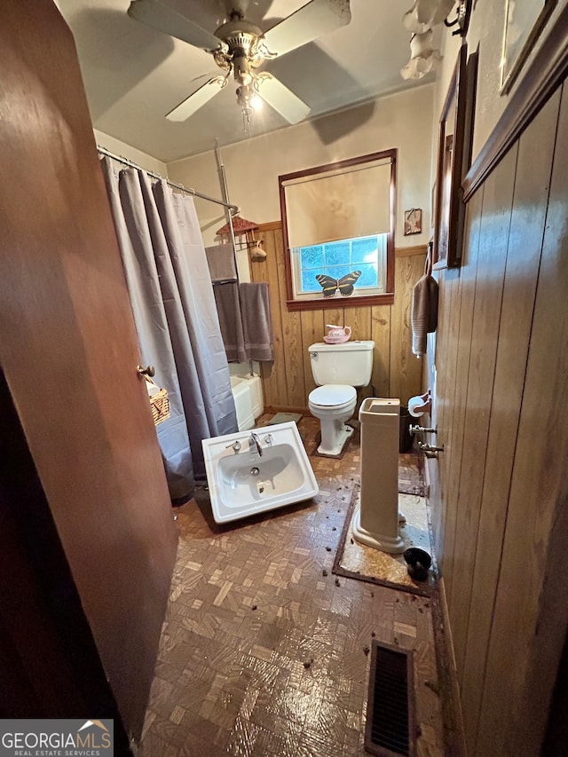 bathroom featuring shower / bath combo, ceiling fan, toilet, and wooden walls