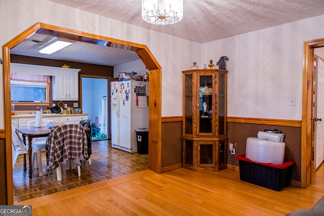 kitchen with white refrigerator with ice dispenser, a textured ceiling, light wood-type flooring, and white cabinetry