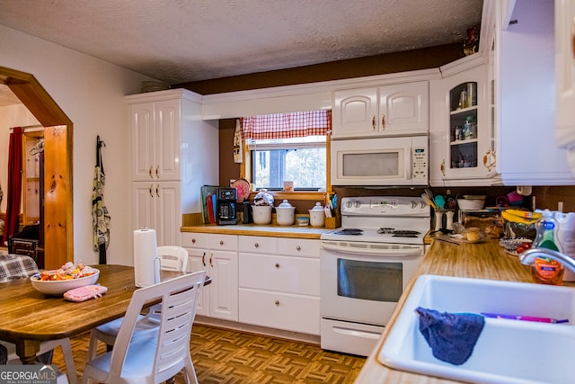 kitchen with sink, parquet flooring, a textured ceiling, white appliances, and white cabinets