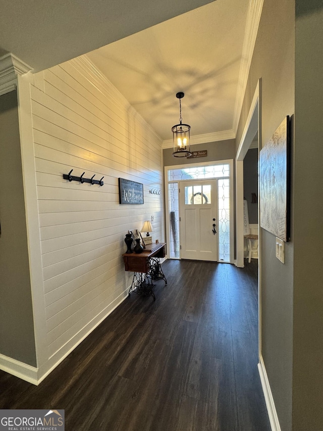 foyer entrance featuring wood walls, an inviting chandelier, dark wood-type flooring, and ornamental molding