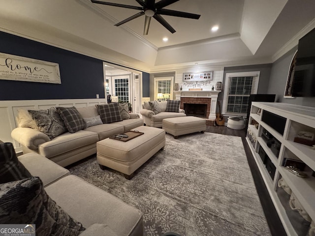 living room featuring ceiling fan, wood-type flooring, ornamental molding, and a brick fireplace