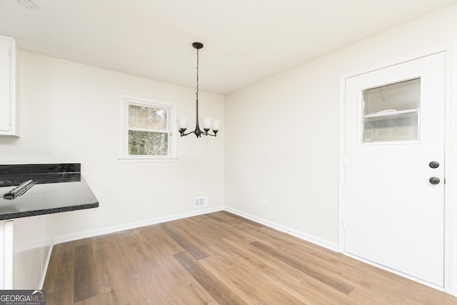 unfurnished dining area with light wood-type flooring and a notable chandelier