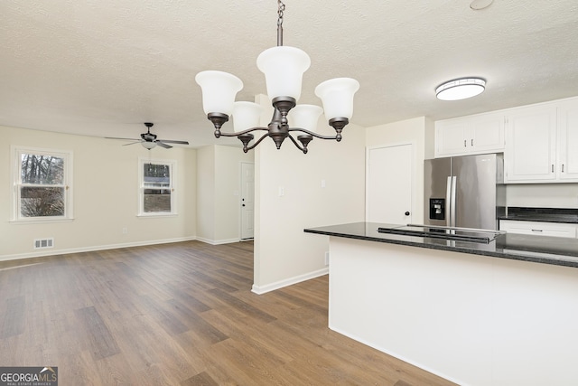 kitchen with decorative light fixtures, stainless steel refrigerator with ice dispenser, black electric cooktop, ceiling fan with notable chandelier, and white cabinets