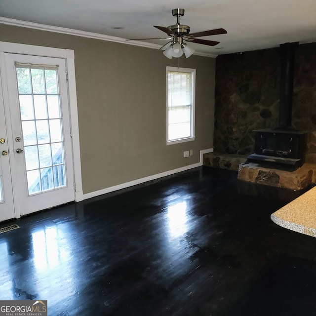 unfurnished living room featuring a wood stove, ceiling fan, dark wood-type flooring, and ornamental molding