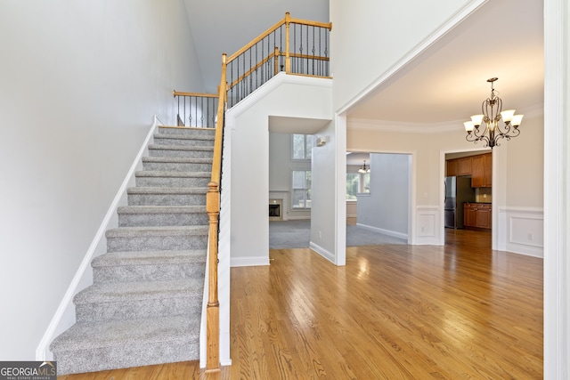 stairs featuring crown molding, a notable chandelier, hardwood / wood-style flooring, and a towering ceiling