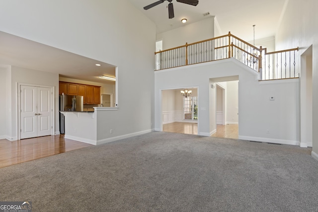 unfurnished living room with carpet flooring, ceiling fan with notable chandelier, and a high ceiling