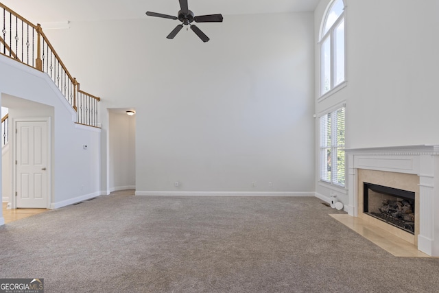 unfurnished living room featuring a premium fireplace, a towering ceiling, light colored carpet, and ceiling fan