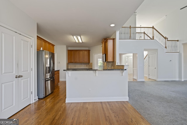 kitchen featuring stainless steel fridge with ice dispenser, backsplash, kitchen peninsula, wood-type flooring, and a breakfast bar