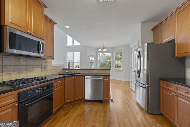 kitchen with sink, stainless steel appliances, tasteful backsplash, a notable chandelier, and light hardwood / wood-style floors