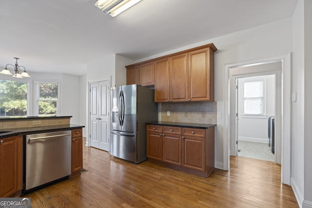 kitchen with an inviting chandelier, dark hardwood / wood-style flooring, backsplash, dark stone countertops, and appliances with stainless steel finishes