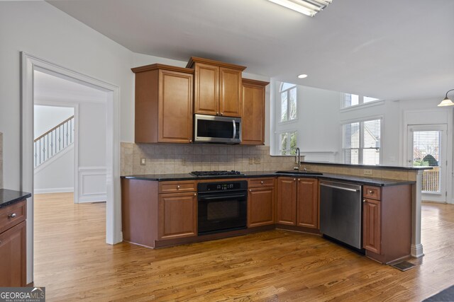 kitchen with kitchen peninsula, tasteful backsplash, sink, black appliances, and hardwood / wood-style flooring