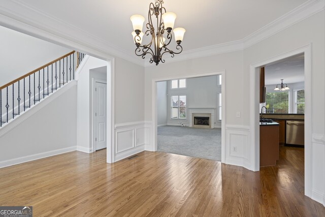 unfurnished dining area featuring hardwood / wood-style floors, crown molding, and an inviting chandelier