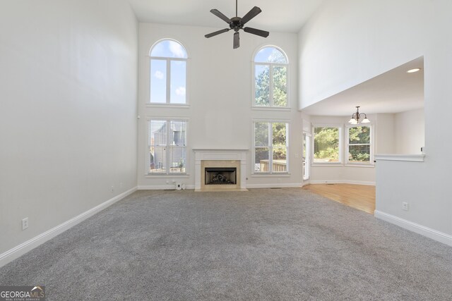 unfurnished living room featuring ceiling fan with notable chandelier, a towering ceiling, a wealth of natural light, and carpet flooring