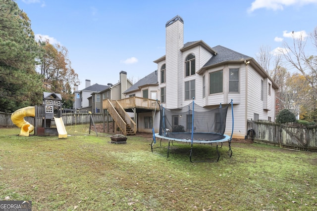 rear view of property with a playground, a wooden deck, a trampoline, and a lawn