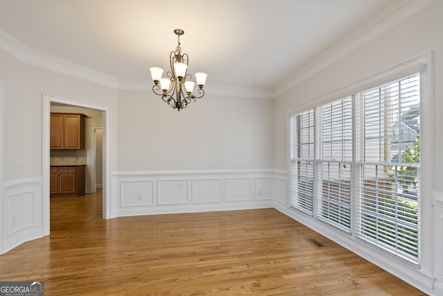 spare room featuring crown molding, light hardwood / wood-style flooring, and an inviting chandelier