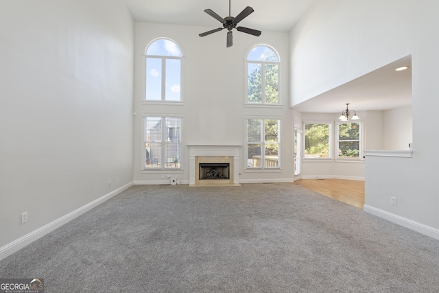 unfurnished living room featuring carpet flooring, plenty of natural light, a towering ceiling, and ceiling fan with notable chandelier