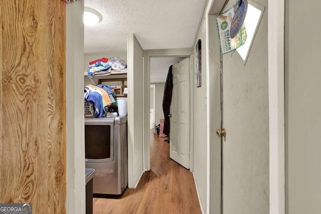 hallway with washer / clothes dryer, light hardwood / wood-style flooring, and a textured ceiling