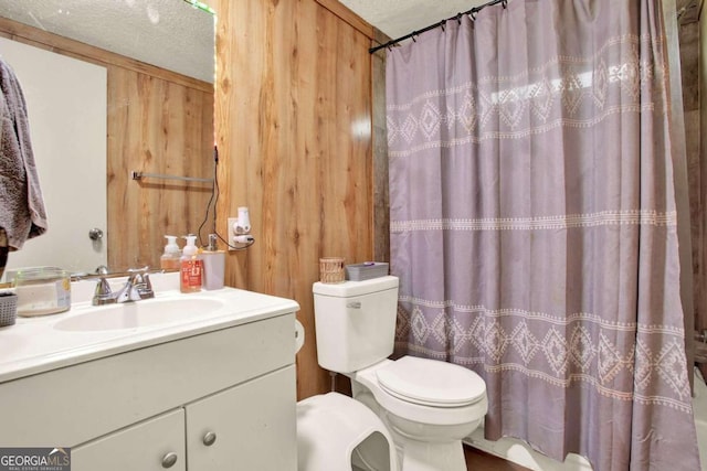 bathroom with vanity, wood walls, toilet, and a textured ceiling