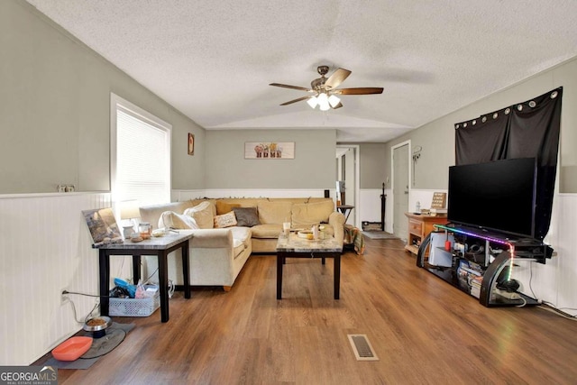 living room featuring lofted ceiling, ceiling fan, wood-type flooring, and a textured ceiling