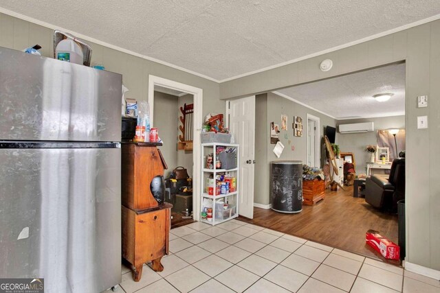 kitchen featuring stainless steel refrigerator, a wall mounted air conditioner, crown molding, a textured ceiling, and light wood-type flooring